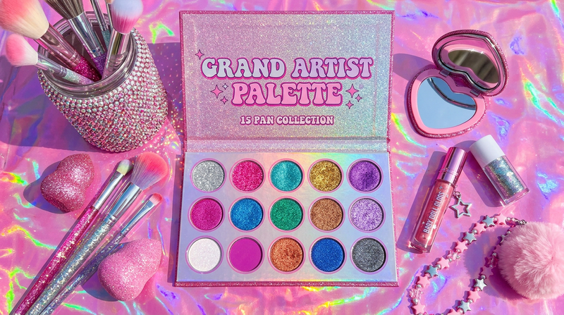 Grand artist palette open with 15 pans surrounded by brushes rhinestone jar on pink holographic vanity