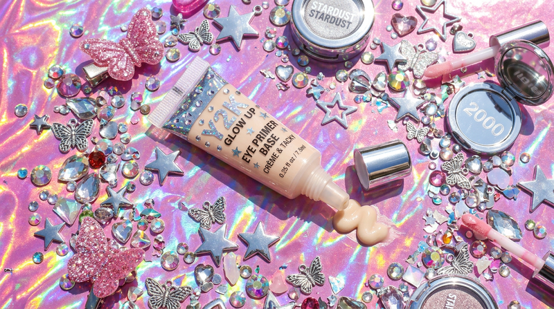 Eye primer base tube flat lay, bubblegum pink holographic background, rhinestone decorations, Y2K Cybrena