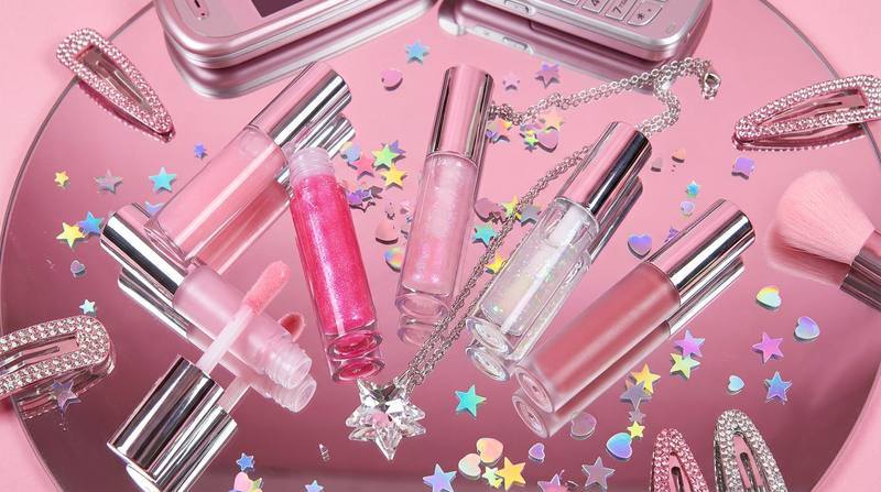 Five Glass Glow lip gloss tubes arranged on pink mirror surface with holographic confetti Y2K maximalist styling